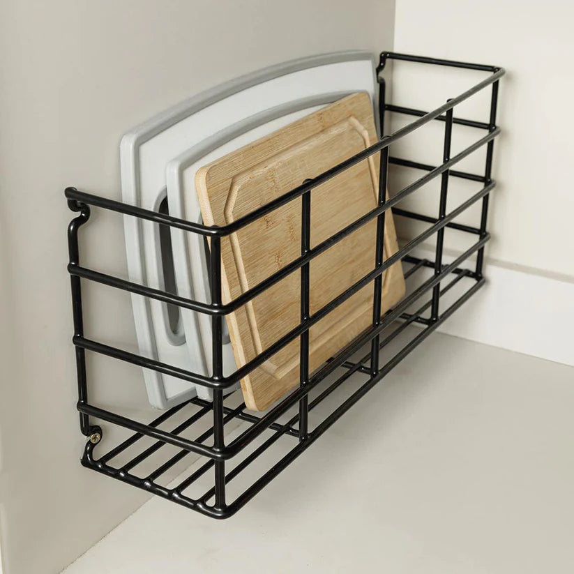 Organizador de tablas de picar en color negro, con tablas junto a una pared blanca