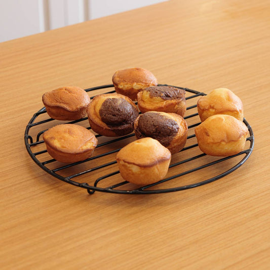 Rejilla de enfriamiento para repostería negra y circular con muffins sobre una mesa de madera
