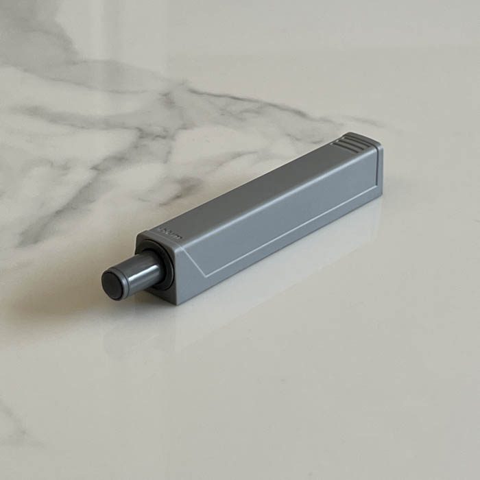 Soporte de amortiguador para puertas de mobiliario y de sistema push to open con el mecanismo insertado sobre fondo claro