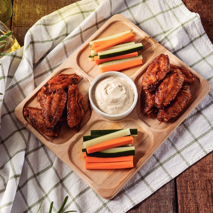 Tabla de piqueo con alitas, verduras y un recipiente de salsa